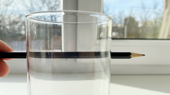 стакан преломляет свет и поэтому карандаш сзади выглядит искажённым